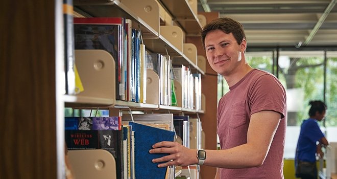 TCC student removes book from library shelf.
