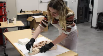 A student glazes the wood body of an electric guitar