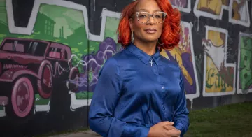 TCC Professor, Corinice Wilson, Ph.D. stands in front of the mural at Black Wall St..