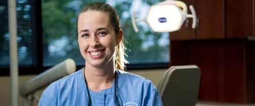 TCC Dental Hygiene student sits in front of dental chair and light.