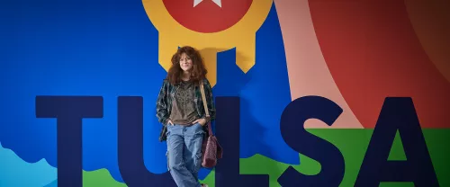 TCC student stands in front of colorful mural reading "Tusla" featuring the Tulsa city seal