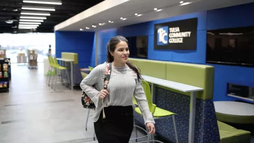 Student walking inside a modern student union on the TCC Southeast campus with lime green seating and a TCC sign on a blue wall.