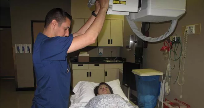 TCC Radiography student positions x-ray machine above a patient who is lying down.