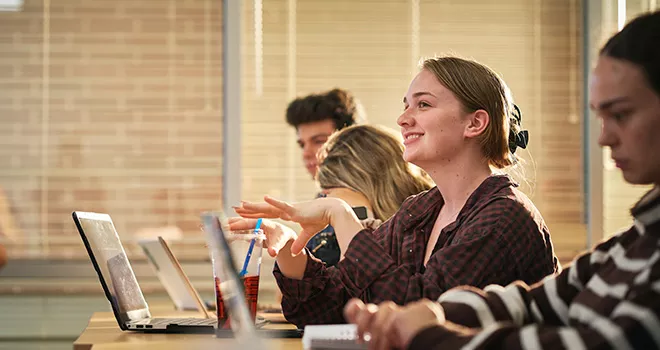 TCC student asks a question in class with a laptop on the desk in front of here.