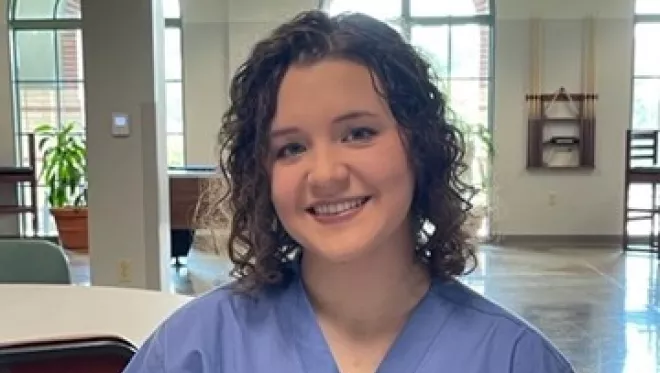 TCC Vet Tech Student sits at a table wearing blue scrubs