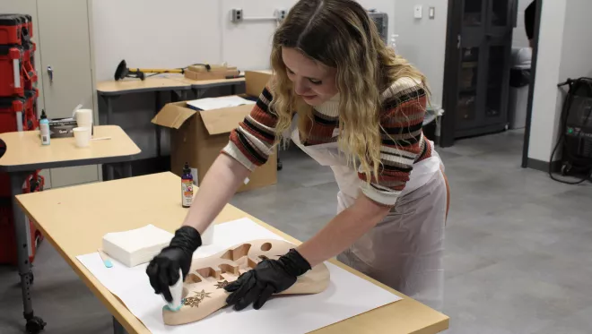 A student glazes the wood body of an electric guitar